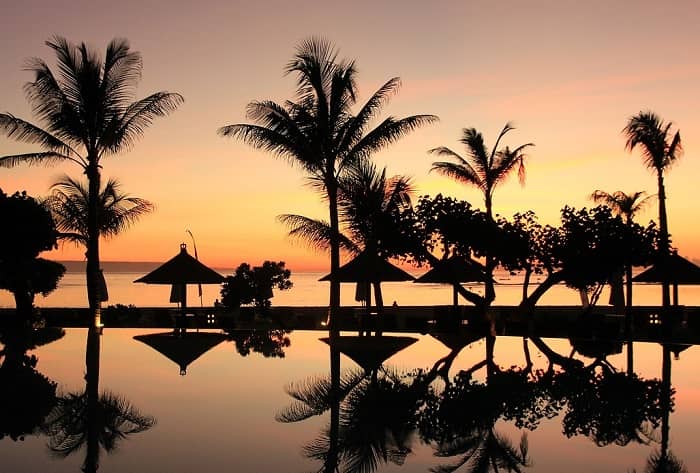 Ein Blick, zwischen Palmen hindurch, in einen Sonnenuntergang auf Bali