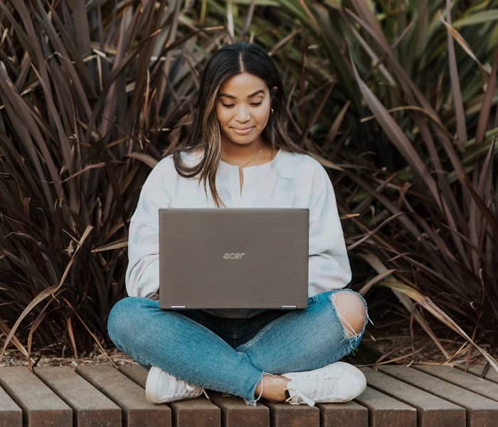 Eine junge Frau sitzt auf einem Holzsteg und tippt auf einem Laptop