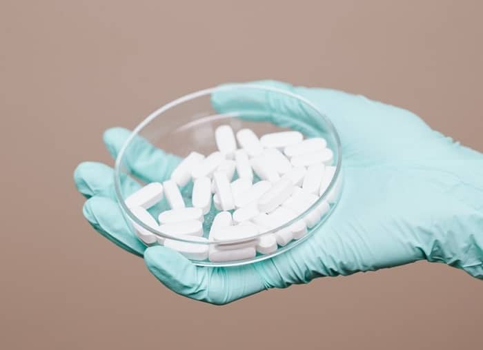 Eine Klinik behandschuhte Hand hält eine Schale mit weißen Pillen