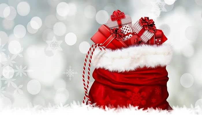 Ein rot-weißer Weihnachtssack steht mit vielen Geschenken vor einer Sternen glitzernden Wand