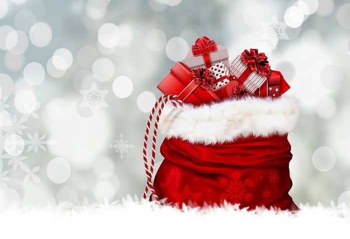 Ein rot-weißer Weihnachtssack steht mit vielen Geschenken vor einer Sternen glitzernden Wand