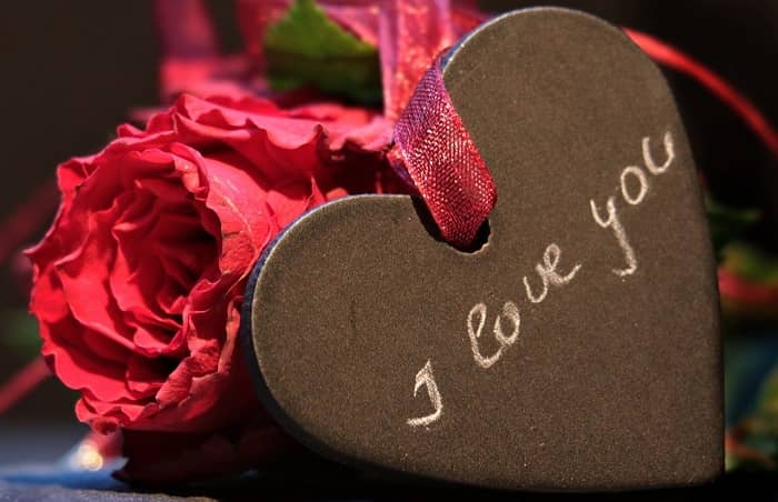 Ein braunes Herz mit der Aufschrift "I love you" liegt vor einem Rosenstrauß