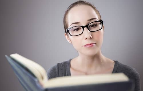 Eine Frau mit Lesebrille liest gerade in einem Buch