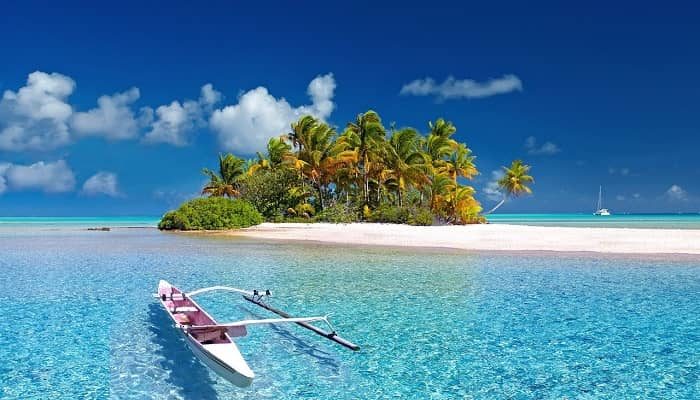 Ein Boot liegt vor einer kleinen Insel mit weißem Sand und Palmen