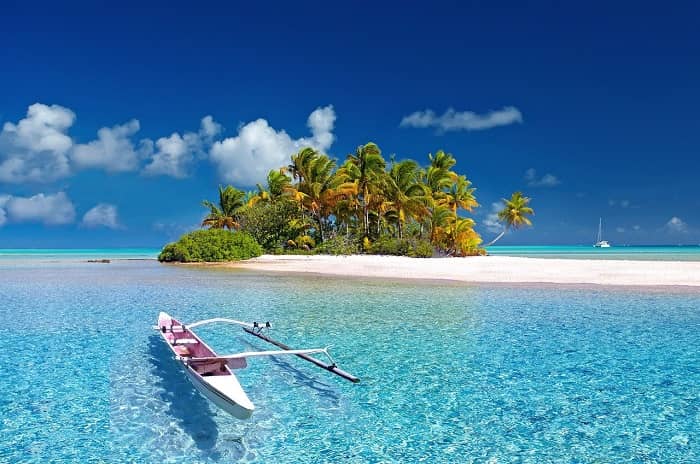 Ein Boot liegt vor einer kleinen Insel mit weißem Sand und Palmen