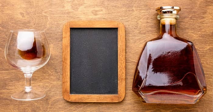 Eine schöne Cognacflasche liegt neben einem Glas und einer Schreibtafel