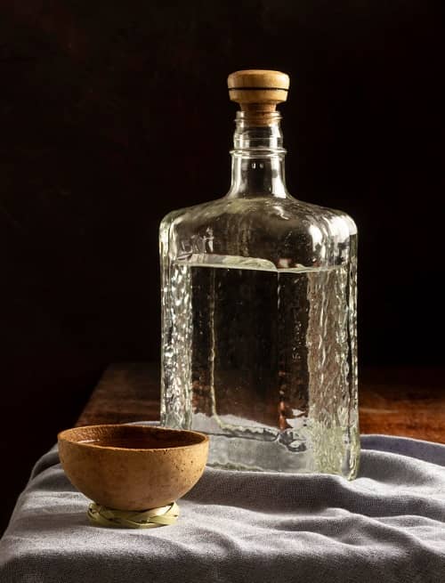 Eine schöne Flasche mit einem klaren Destillat darin, steht mit einer Trinkschale auf einem Tisch
