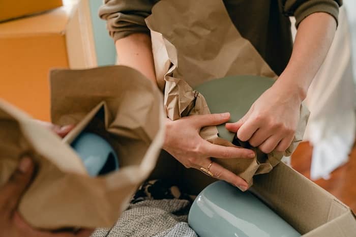 Zwei Personen verpacken Geschirr mit Packpapier