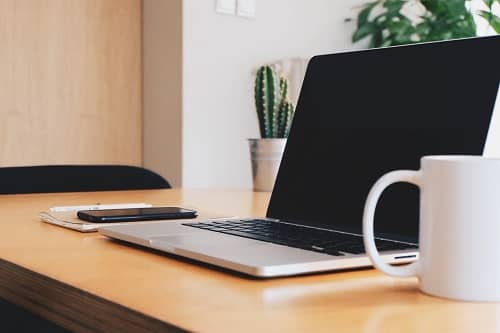 Ein Laptop steht mit einer Kaffeetasse auf einem Schreibtisch