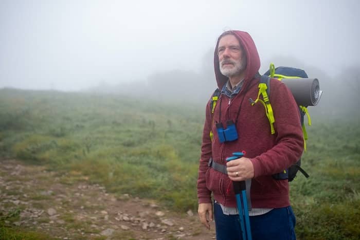 Ein Wanderer steht im Nebel auf einem Weg, im Hintergrund sieht man Berge