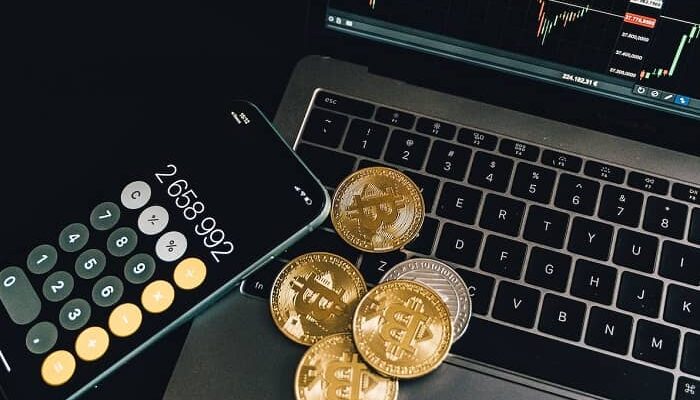 Auf einem Laptop liegen verschiedene Bitcoin Münzen und ein Handy mit geöffnetem Taschenrechner