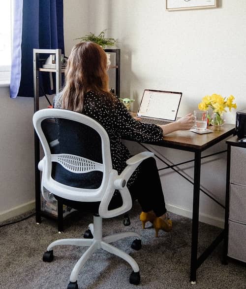 Eine Frau sitzt auf einem ergonomischen Bürodrehstuhl an Ihrem Schreibtisch vor dem Laptop