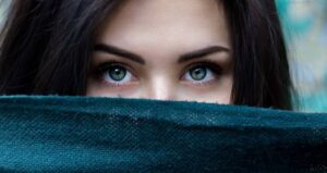 Ein Frauengesicht, das zur Hälfte mit einem Schal bedeckt ist, die Augen wirken sehr dominant