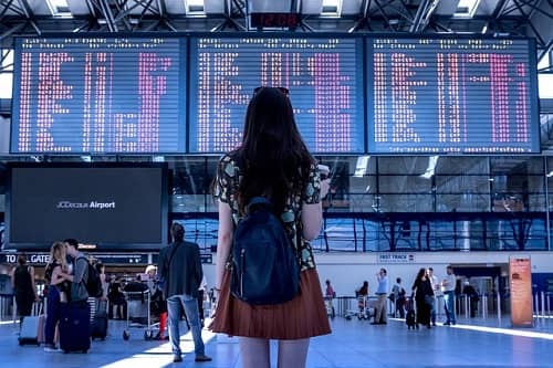 Frau mit Rucksack steht vor einer Abflugtafel im Flughafen