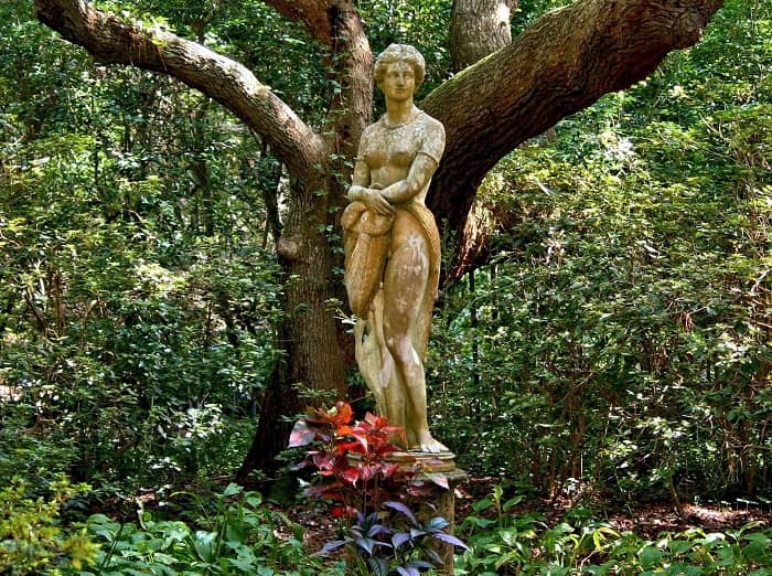 Eine weibliche Skulptur steht vor einem bizarr geformten Baum
