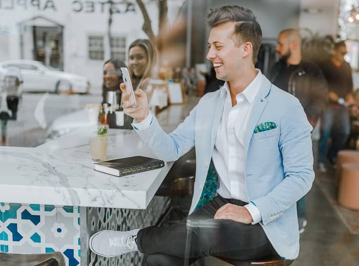 Ein junger, sehr gut gekleideter Mann sitzt an einer Bar und schaut auf sein Smart Phone