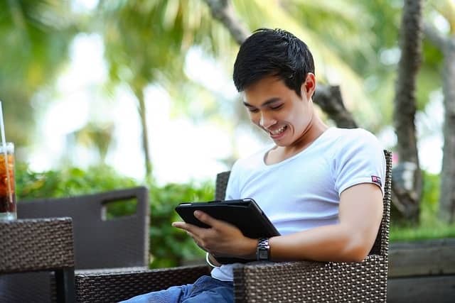 Ein junger Mann sitzt mit einem Tablett im Garten und liest Nachrichten