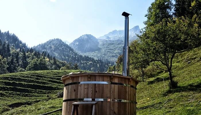 Ein Badezuber steht auf einer Hangwiese mitten in den Bergen