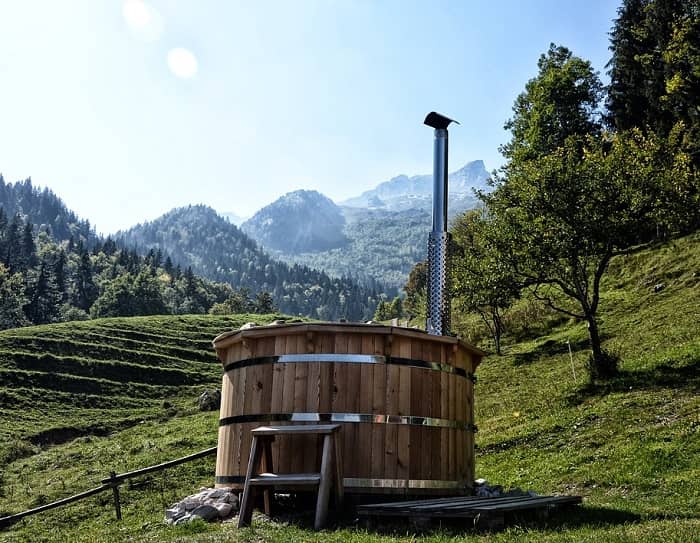 Ein Badezuber steht auf einer Hangwiese mitten in den Bergen