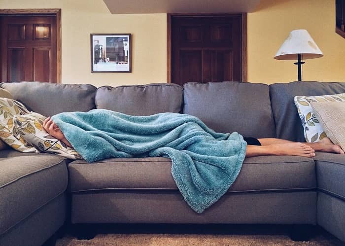 Ein Mann liegt tagsüber auf einem Sofa, komplett mit einer Decke zugedeckt