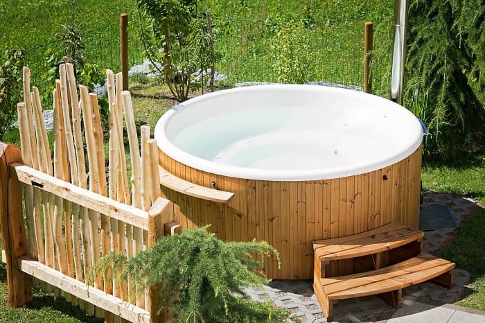 Ein Whirlpool steht in einem Garten, umgeben von Büschen und Wiese