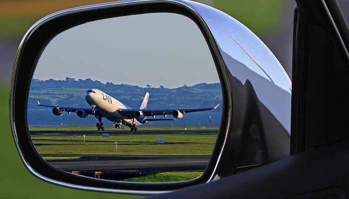 In einem Autoseitenspiegel sieht man ein Flugzeug starten