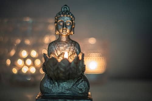 Eine kleine Buddha Figur sitzt und hält eine Kerze in Händen