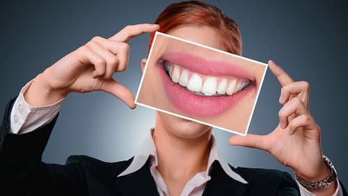 Eine Frau hält ein Plakat mit sehr schönen Zähnen vor Ihr Gesicht