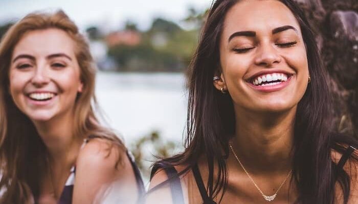 Zwei Mädchen sitzen lächelnd mit weißen Zähnen am See