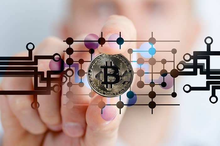 Eine Hand hält eine Bitcoin Münze vor ein Digitales Schaubild