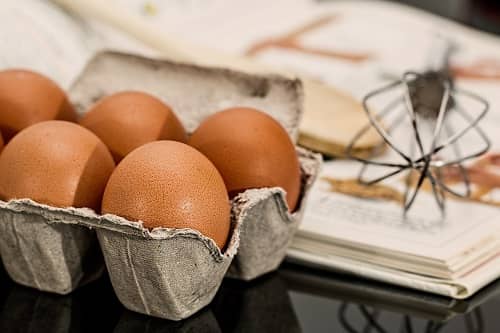Eier neben einem Schneebesen und einem Kochbuch