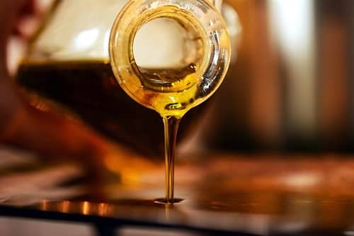 Aus einer Glasflasche fließt Olivenöl in einen Behälter