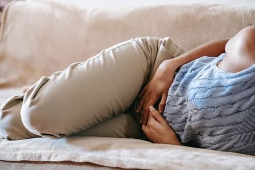 Eine Frau liegt auf einem Sofa und hat Bauchschmerzen