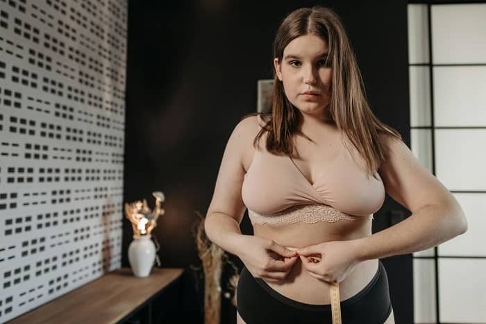 Eine junge Frau mit einem Massband misst Ihre Körperfülle