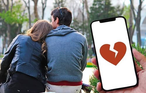 Ein Paar sitzt auf einer Bank, daneben ein Handy, auf dem ein gebrochenes Herz abgebildet ist.