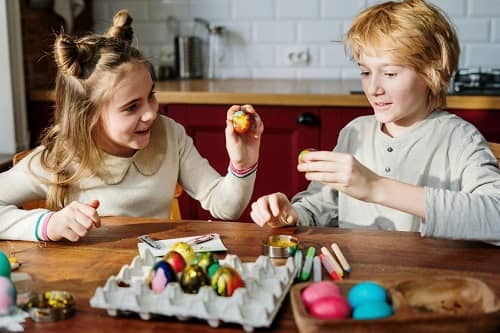 Zwei Kinder sitzen in der Küche und spielen Ostereierschlagen