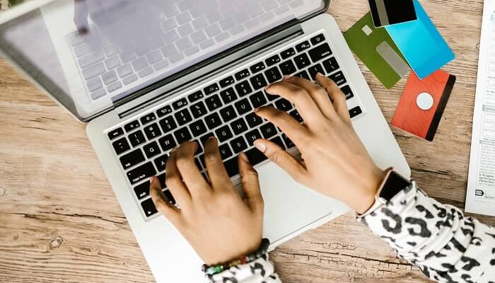 Eine Frau tippt auf Ihrem Laptop und bestellt etwas, daneben liegen verschiedene Kreditkarten