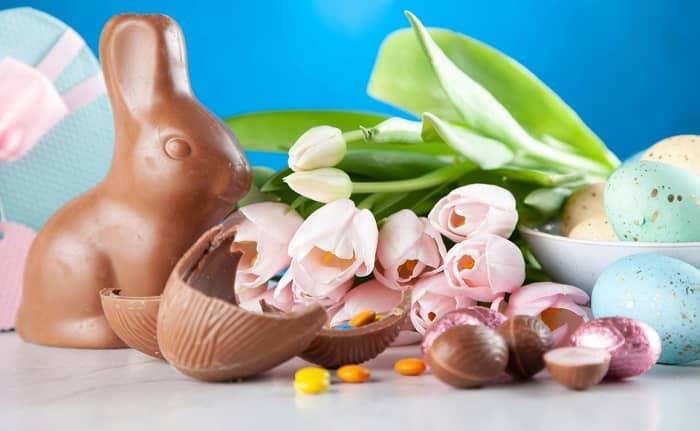 Ein Schokoladenosterhase steht neben Tulpen und einem Korb mit Ostereiern