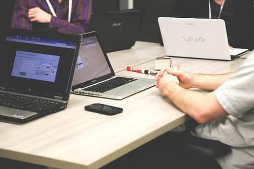 Männer sitzen um einen Schreibtisch und arbeiten mit Ihren Laptops