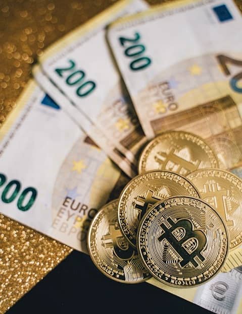 Euroscheine und goldene Bitcoinmünzen liegen auf einem Tisch.