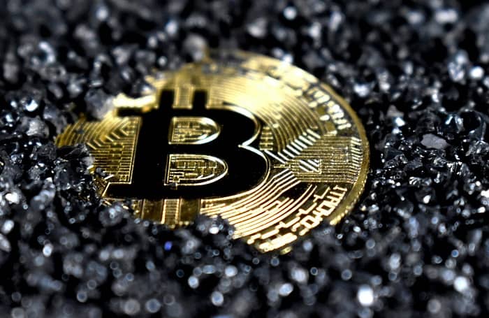 Eine Bitcoin Goldmünze liegt in schwarzem Zierkies
