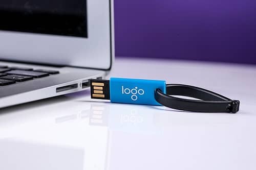 Ein USB Stick mit modernem Aufdruck liegt neben einem Laptop