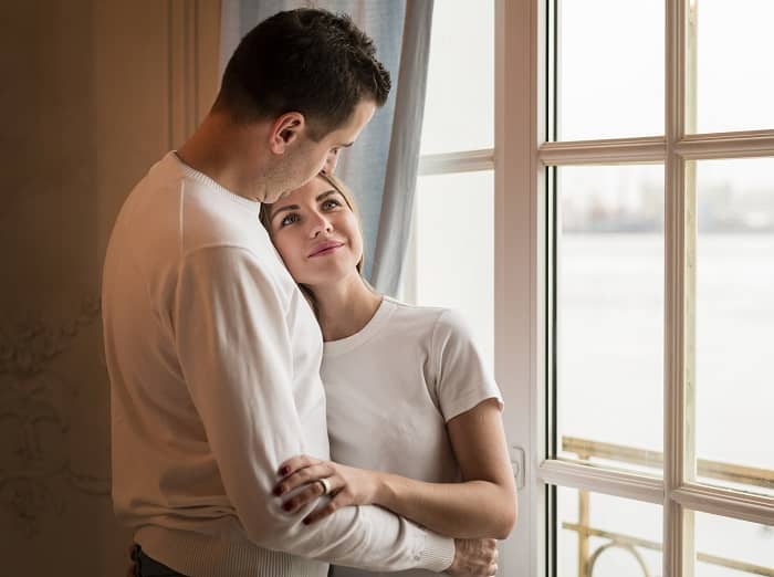 Ein Mann umarmt eine Frau direkt vor einem großen Fenster