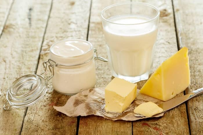 Ein Glas Milch und Butter mit einem Stück Käse auf einem Holztisch