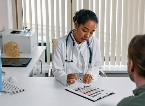 Eine Ärztin geht im Sprechzimmer einen Diagnose Bogen mit einem Patienten durch
