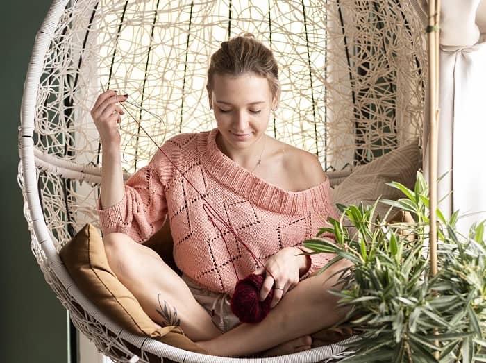 Eine Frau sitzt in einer geflochtenen Hängeschale und strickt